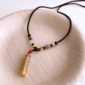 Detail of golden cylinder pendant with engraved scriptures and multi-color beaded rope