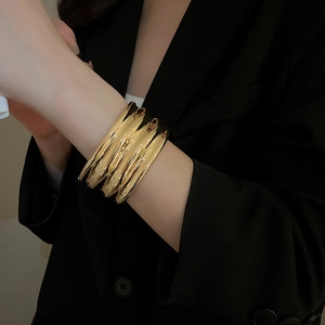 Detail shot of chunky gold irregular textured bangle on a model's wrist in black suit