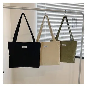 Three corduroy tote bags in black, beige, and olive green hanging with fashion labels