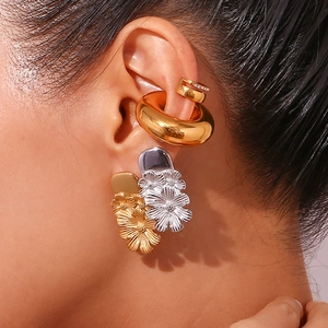 Detail of layered gold earrings featuring daisy charm and chunky hoop on ear