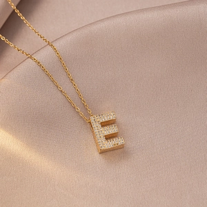 Macro shot of gold letter E pendant necklace with sparkling cubic zirconia on silk