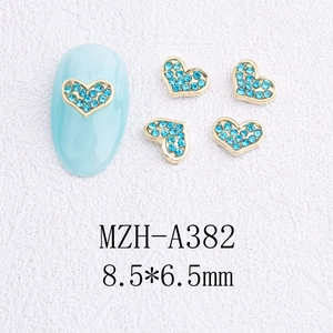 Vue détaillée de bijoux d'ongles cœur doré avec strass bleus sur un ongle manucuré