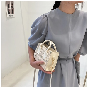 Detail of floral embroidery on a white woven straw handbag with faux leather handle and gold hardware