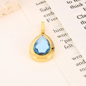Macro shot of a golden teardrop pendant with a pear-cut blue gemstone on a book