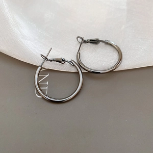 Close-up of minimalist gunmetal hoop earrings with polished finish on grey silk fabric