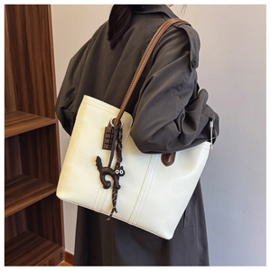 Detailed close-up of a cream tote bag featuring dark brown cat charms and fine stitching