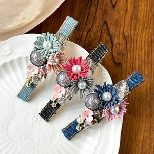 Detailed view of three denim fabric hair clips with floral and pearl accents on ceramic