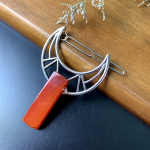 Detailed shot of silver crescent moon hair clip with orange crystal on wood