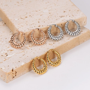 Textured twist hoop earrings in gold, silver, and rose gold on a stone pedestal