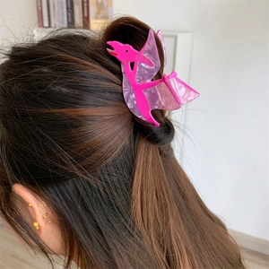Detail view of a cute pink dinosaur acrylic hair claw clip worn on model's hair