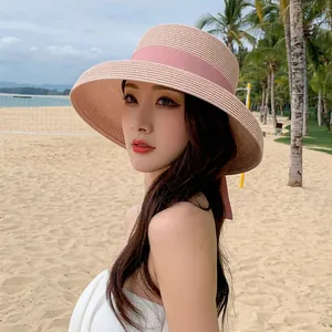 Elegant wide-brim pink straw sun hat with ribbon on beach background