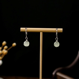 Detailed close-up of pale green jade earrings with silver hooks on a golden display stand