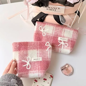 Detail of pink plaid plush makeup bags with ribbon bows and brand labels on pink gift box