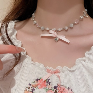 Close-up of a beaded choker featuring a pink satin bow and silver heart pendant on a model