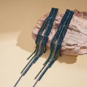 Macro view of long fringe earrings with blue and green rhinestones on stone background
