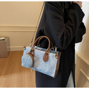 Detail of blue denim tote bag with brown leather trim and round zipper charm