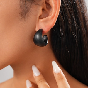 Close-up of minimalist black acrylic C-shape hoop earrings worn by a model in dark style