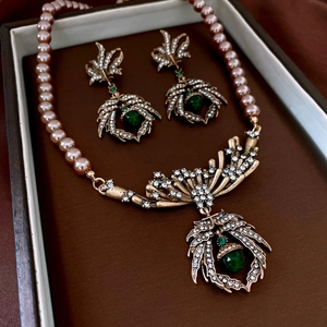 Detail of luxury jewelry set featuring pink pearls and green gemstone leaf pendant