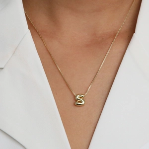 18k gold bubble letter S pendant necklace worn by model on a white blazer background