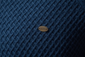 Macro view of dark blue waffle knit texture with vintage gold metal brand emblem