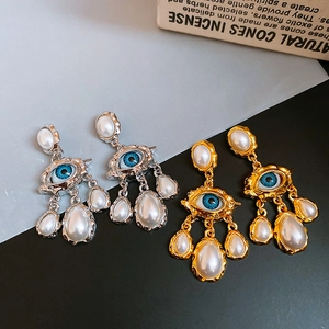 Macro shot of surrealist eye earrings with blue pupils and teardrop pearls in gold and silver