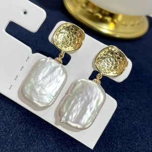 Elegant gold earrings with large baroque pearls on a textured deep blue background