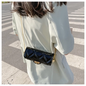 Close-up of black quilted cylinder jelly bag with metallic chain and clasp on street