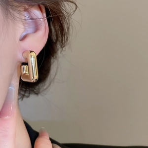 Gros plan d'élégantes boucles d'oreilles rectangulaires dorées en U sur un mannequin