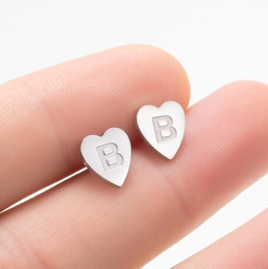 Vue macro de boucles d'oreilles cœur argentées avec gravure B et texture en métal brossé