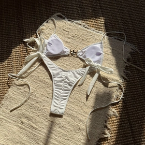 Detail of white bikini with golden starfish hardware on textured woven fabric background