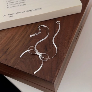 Detailed view of silver bow bracelet with flat blade chain and lobster clasp on dark wood box