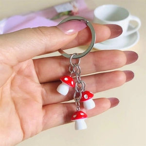 Detail of red and white resin mushroom charms on a metal keychain held by hand