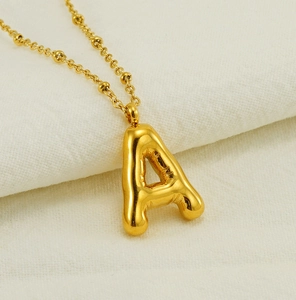 Macro view of gold bubble letter A pendant on a bead chain over beige fabric