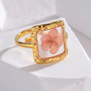 Detail of gold open ring with a pink dried flower set in a square hammered resin frame