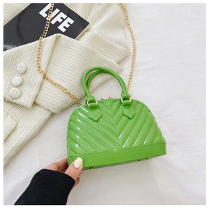 Detail of lime green jelly shell bag with gold chain strap on a white textured background