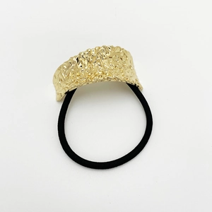 Detail of golden hammered metal plate on black elastic hair tie with reflective texture