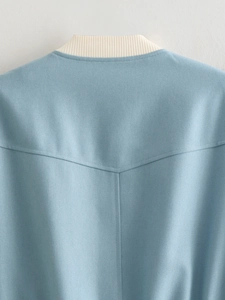Detail shot of blue twill jacket featuring cream rib-knit stand collar and fine stitching