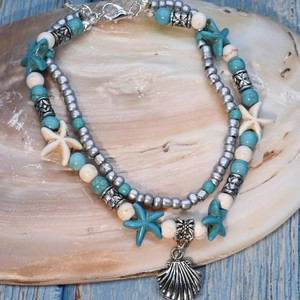 Detail of beaded layered anklet with starfish and shell charms on a wooden surface