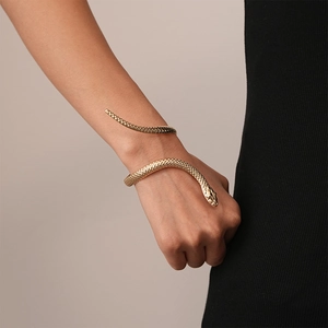 Detail of gold snake-shaped bangle with textured scales on model's wrist with black knit