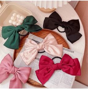 Detailed view of oversized satin bow hair ties in five colors on a wooden tray