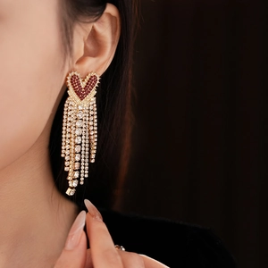 Close-up of gold heart earrings with red rhinestones and elegant white tassel chains