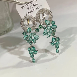 Détail macro de boucles d'oreilles en argent avec pierres émeraude et pompons de zircon
