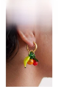Detail of creative fruit charms earrings with banana and cherry on gold hoops
