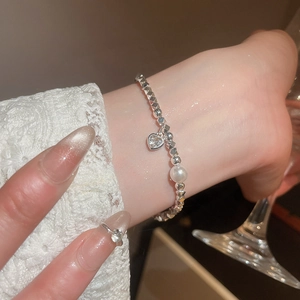 Primo piano del bracciale in argento con ciondolo a cuore e perla su polsino in pizzo
