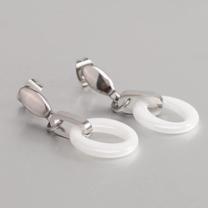 Close-up of silver steel dangling earrings with white ceramic round pendant details