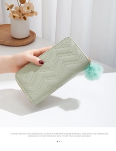 Light green long quilted wallet with pompom pendant held by a model in a cozy setting