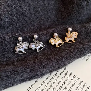 Pony earrings with pearls and cubic zirconia in gold and silver finish on a book