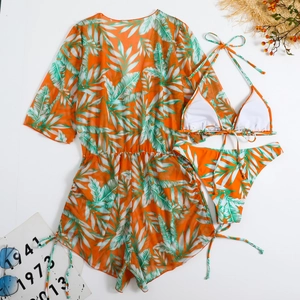 Flat lay of a three-piece orange bikini set with tropical green palm leaf prints and mesh cover-up
