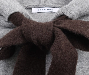 Close-up of grey knit sweater neckline featuring a dark brown decorative bow and brand label