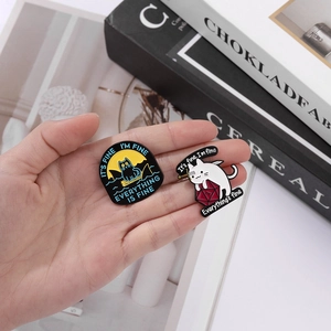 Handheld view of two cat enamel pins with humorous quotes and d12 dice design